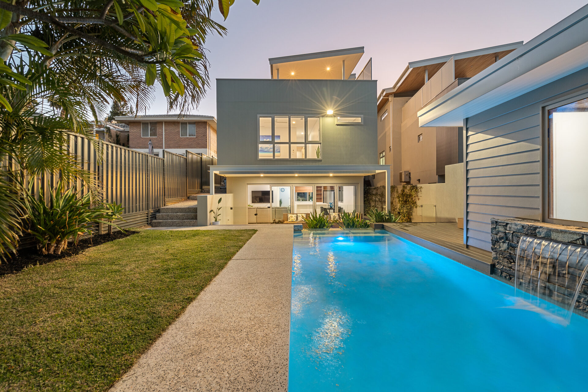 Contemporary two-storey coastal home at dusk with a swimming pool and landscaped backyard