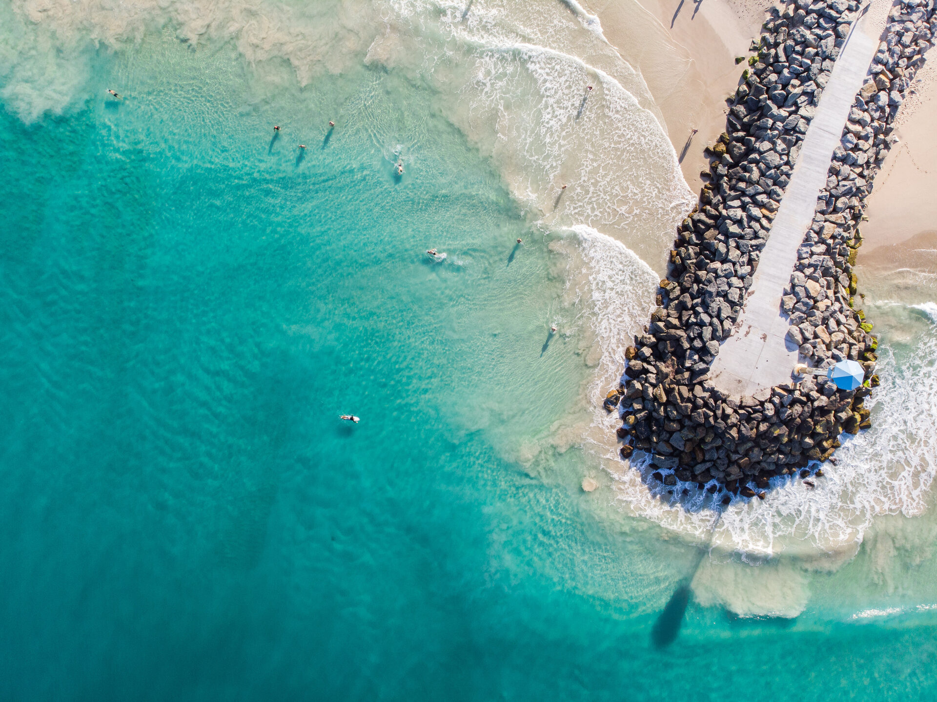 Aerial view of a Perth coastal groyne and beach with surfers in turquoise water